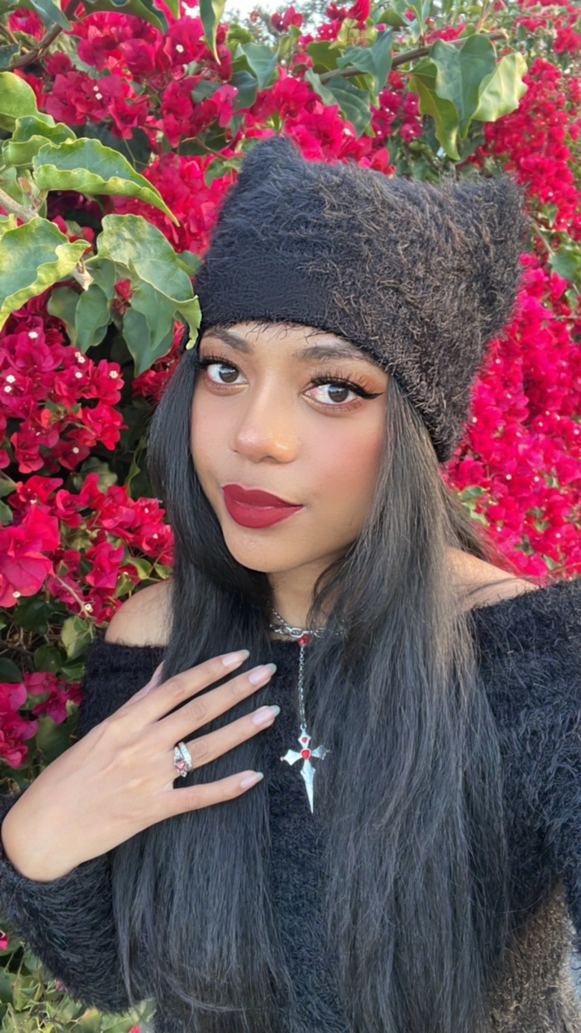Woman wearing a black knit hat and sweater with red flowers in the background